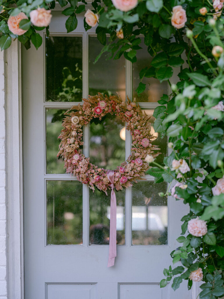 Abraham Darby | English Shrub
David Austin Roses floral wreath hanging on a white door and framed by blush roses.