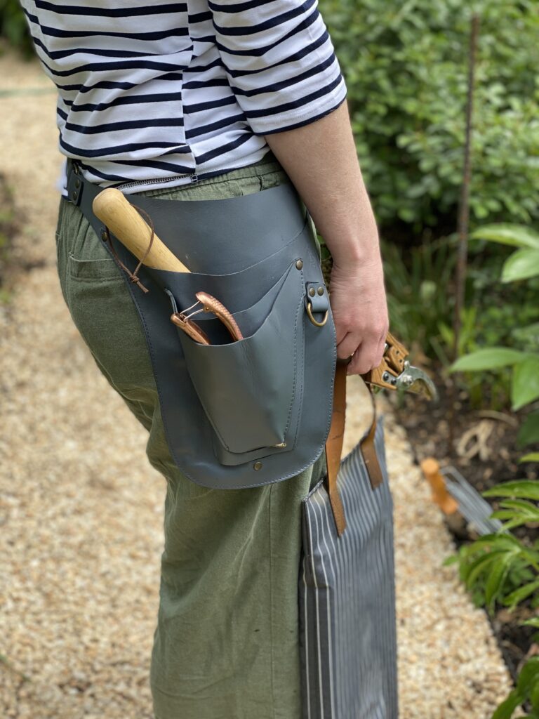 Laura Hooper wearing her custom grey gardening tool belt with tools inside at Foxhill Garden
