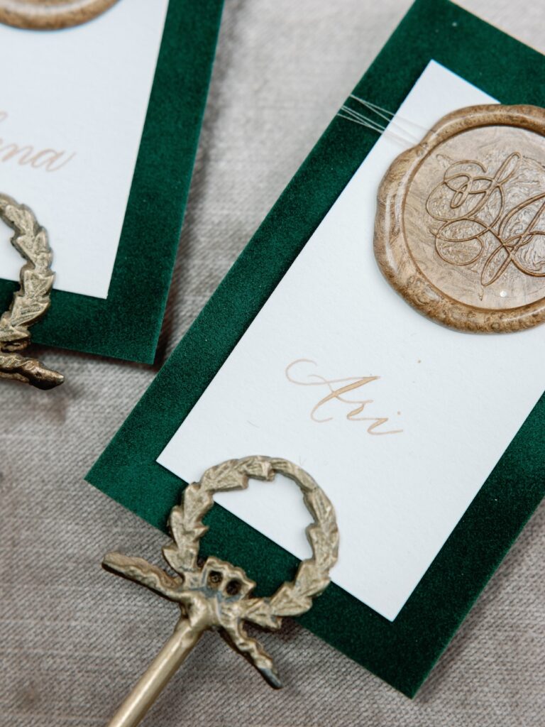 Custom wedding escort cards with gold calligraphy, green velvet and wax seal by Laura Hooper Design House