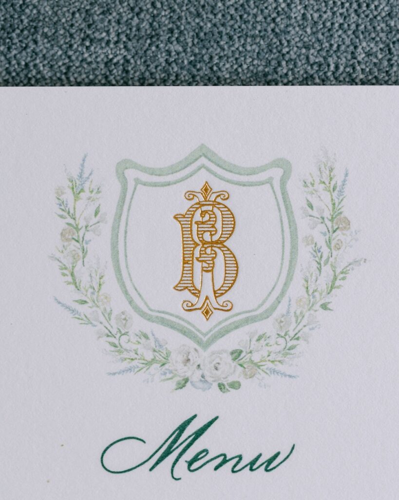 Gold foil monogram crest shield with custom watercolor floral border wedding menu. Laura Hooper Design House.