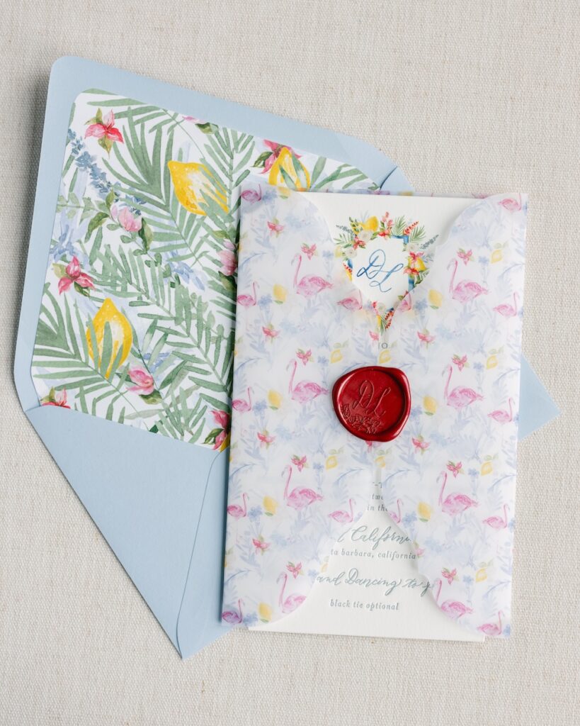 Custom watercolor wedding invitation suite with floral monogram crest, flamingo patterned vellum wrap with custom wax seal, tropical watercolor envelope liner. Laura Hooper Design House.